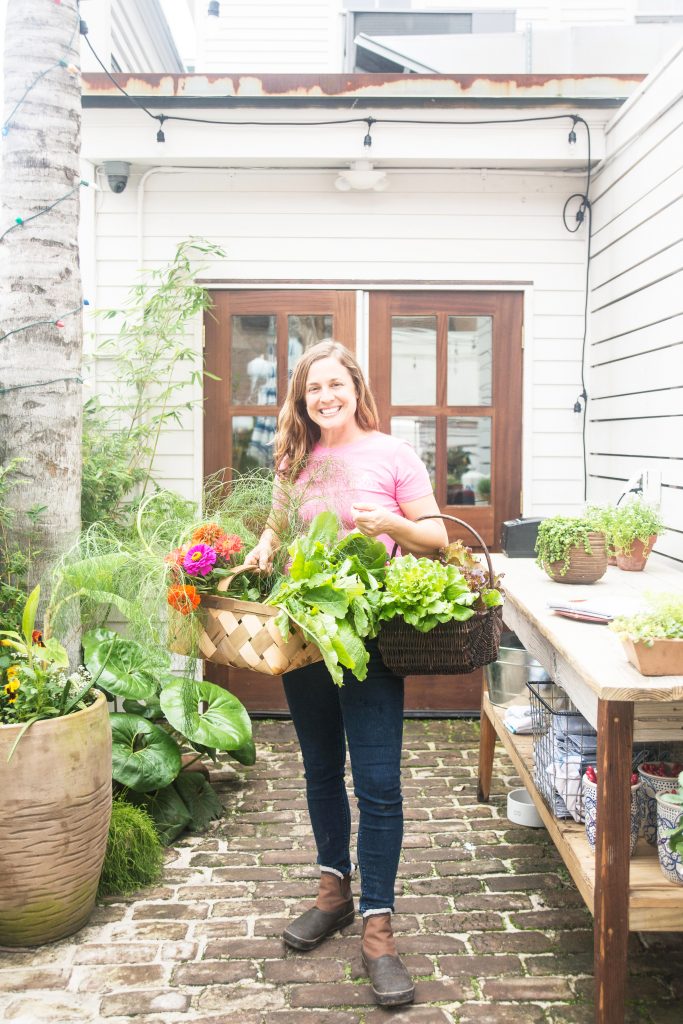 Rita Bachmann stands holding baskets of produce.